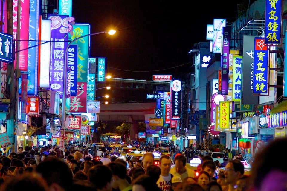 A crowded street at night with neon signs and billboards.