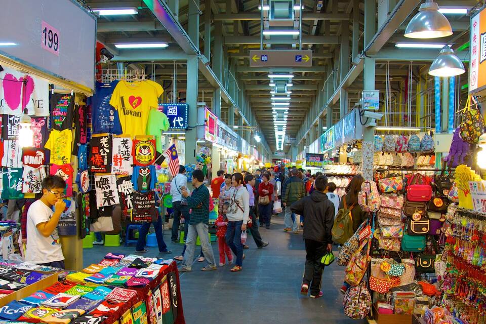 A bustling indoor market with various stalls selling colorful merchandise, including bags and clothing.