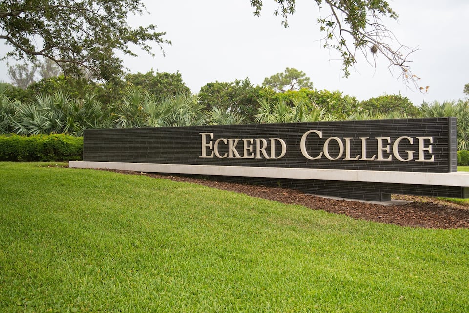 Un panneau indiquant l’entrée de l’université Eckerd, avec un champ verdoyant et des arbres en arrière-plan.