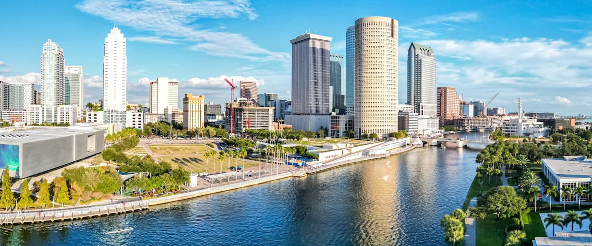 A city skyline with modern high-rise buildings, a river, and a bridge.