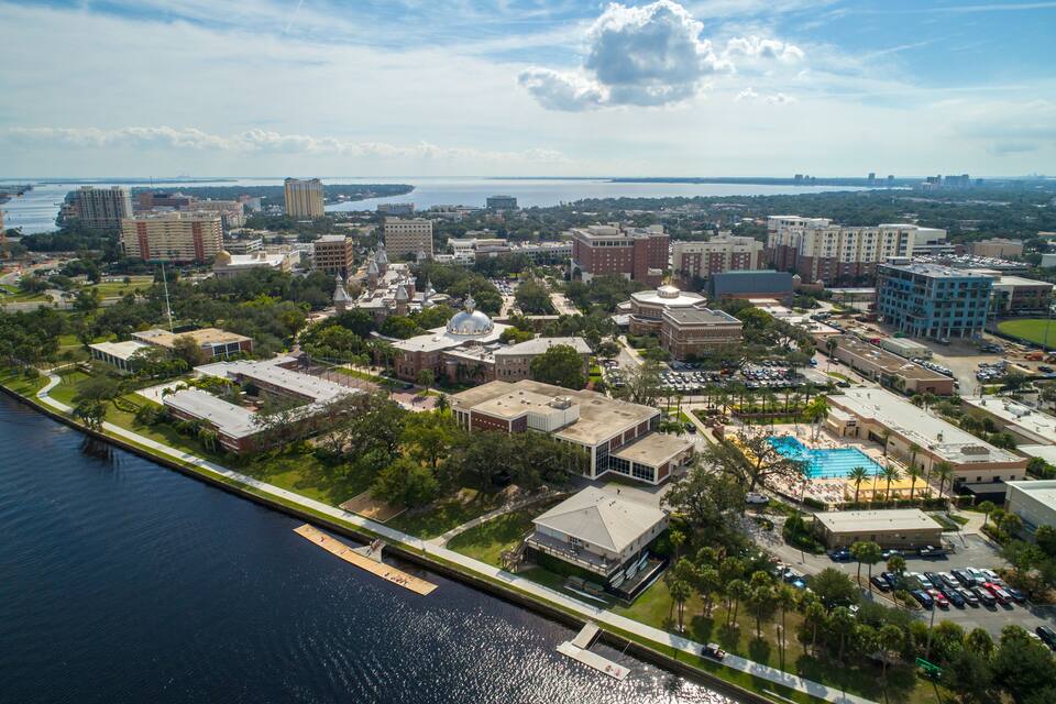 An aerial view of a coastal city with a marina, buildings, and a large swimming pool.