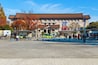 Ein traditionelles Gebäude mit einem Ziegeldach, einem grün-gelben Auto und Menschen, die auf einem Platz spazieren.