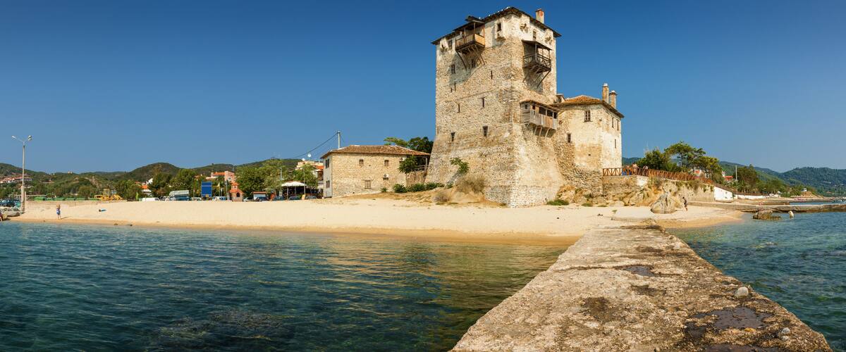 A coastal castle with a tower, beach, and clear waters.