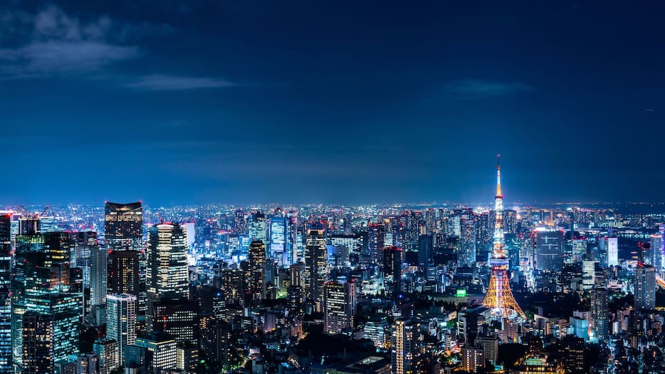 Silhueta urbana densa à noite, com muitos edifícios iluminados e uma torre imponente com um pináculo.