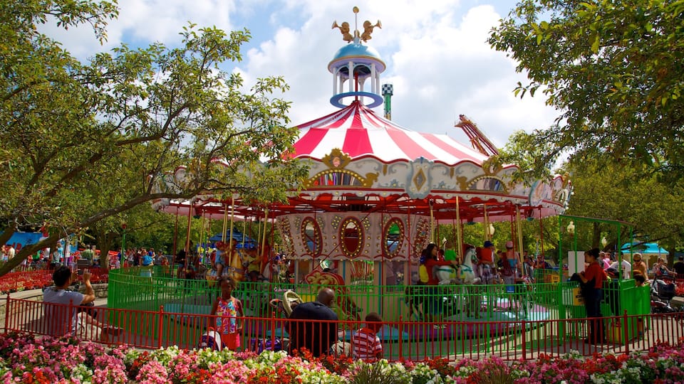 A carousel with a red and white striped canopy, surrounded by a green fence and colorful flowers.
