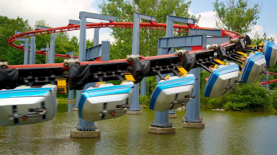 A roller coaster with blue and white cars, red tracks, and a water body in the foreground.