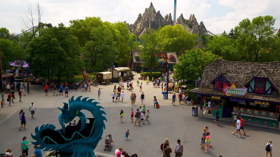 A bustling theme park with a large dragon statue, a roller coaster, and a mountain backdrop.