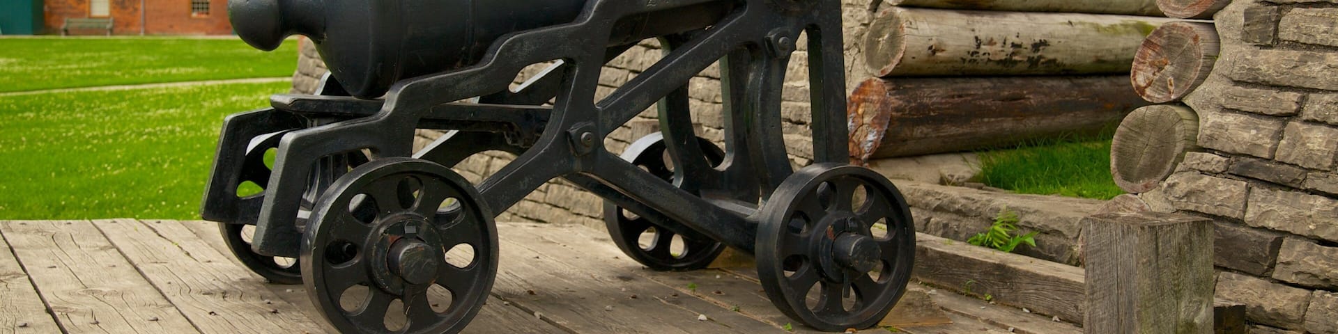 A black cannon on a wooden platform with wheels, set against a brick building with chimneys and a Canadian flag.