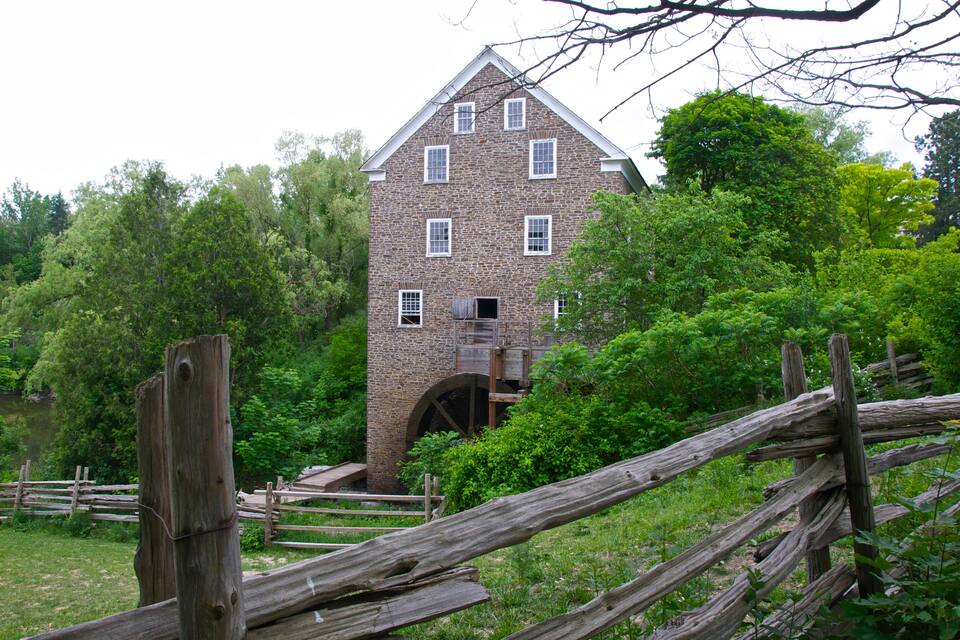 A stone building with a wooden staircase and a large water wheel.