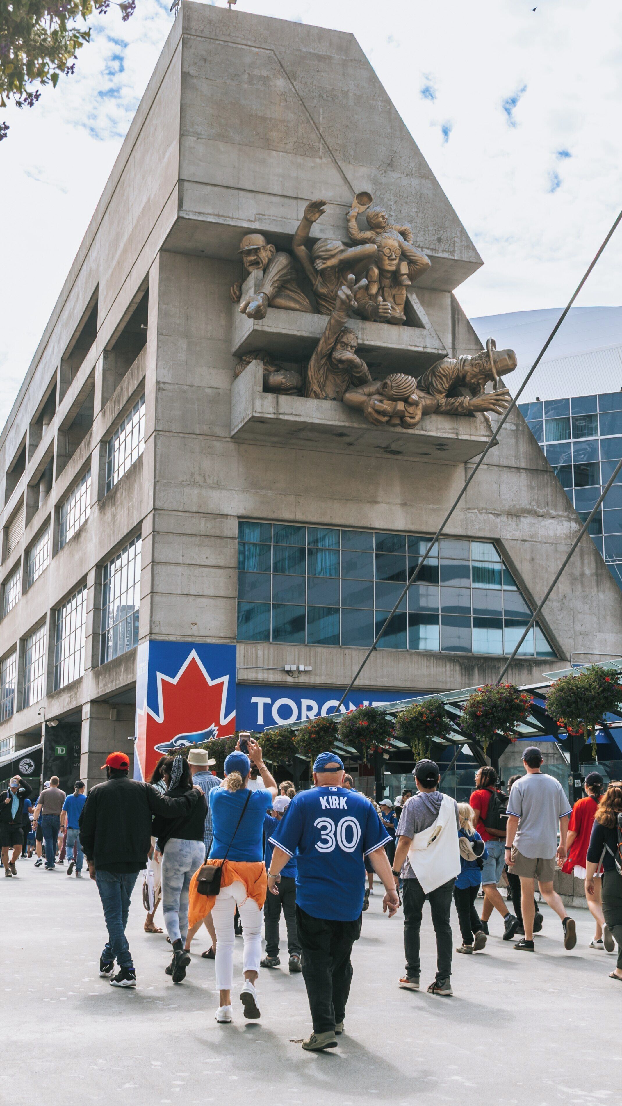 Visitors explore the exterior of Rogers Centre in Toronto's Entertainment District, showcasing its unique architectural design and lively atmosphere during a bustling summer day