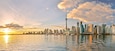 A city skyline with a prominent tower, reflecting on calm water during sunset.