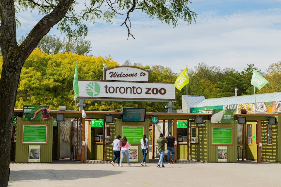 De ingang van de Toronto Zoo, met een bord, groene poorten en bezoekers.