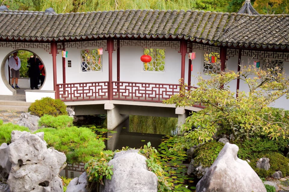 A traditional Chinese building with a tiled roof, red pillars, and a stone bridge over a pond.