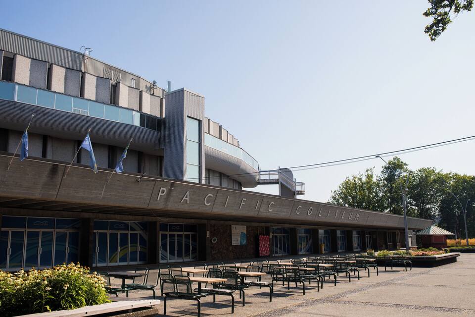 The Pacific Coliseum building with outdoor seating and flags.
