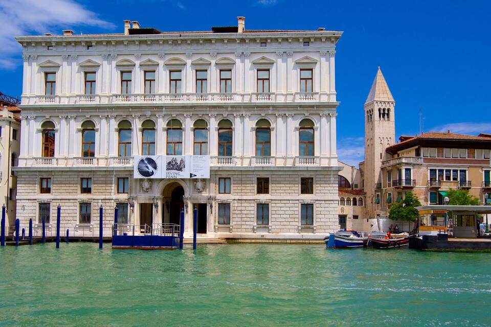 A historic building with a prominent tower, a waterfront, and traditional Venetian architecture.