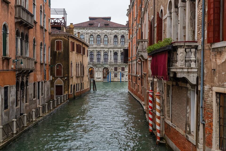Un canal estret a Venècia, Itàlia, flanquejat per edificis històrics amb finestres i balcons arquejats.