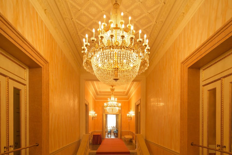 Un vaste hall d’entrée agrémenté d’un grand lustre, de portes richement décorées et d’un tapis rouge.