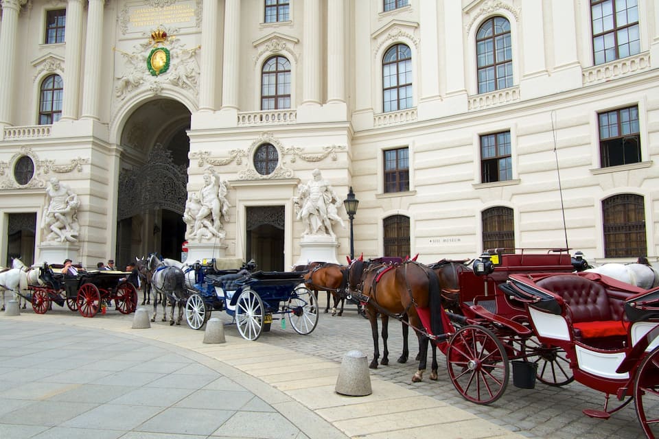 A historic building with ornate sculptures and a horse-drawn carriage in front.