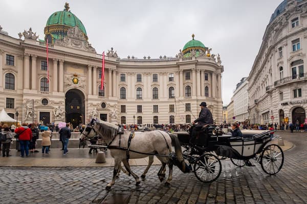 Un edificio histórico con arquitectura ornamentada y un carruaje tirado por caballos frente a él.