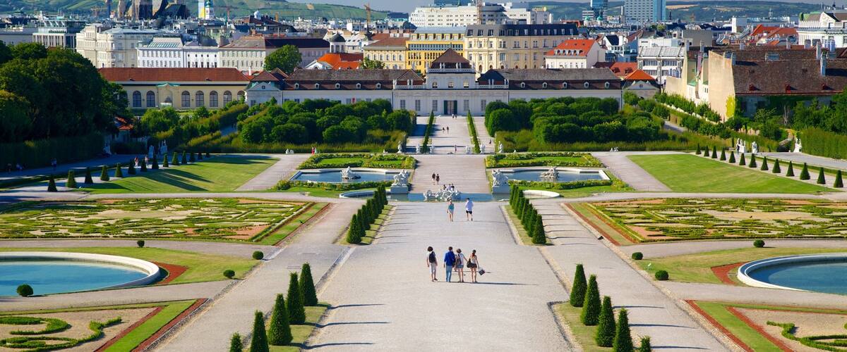 A grand palace with symmetrical gardens, a large fountain, and a distant church spire.