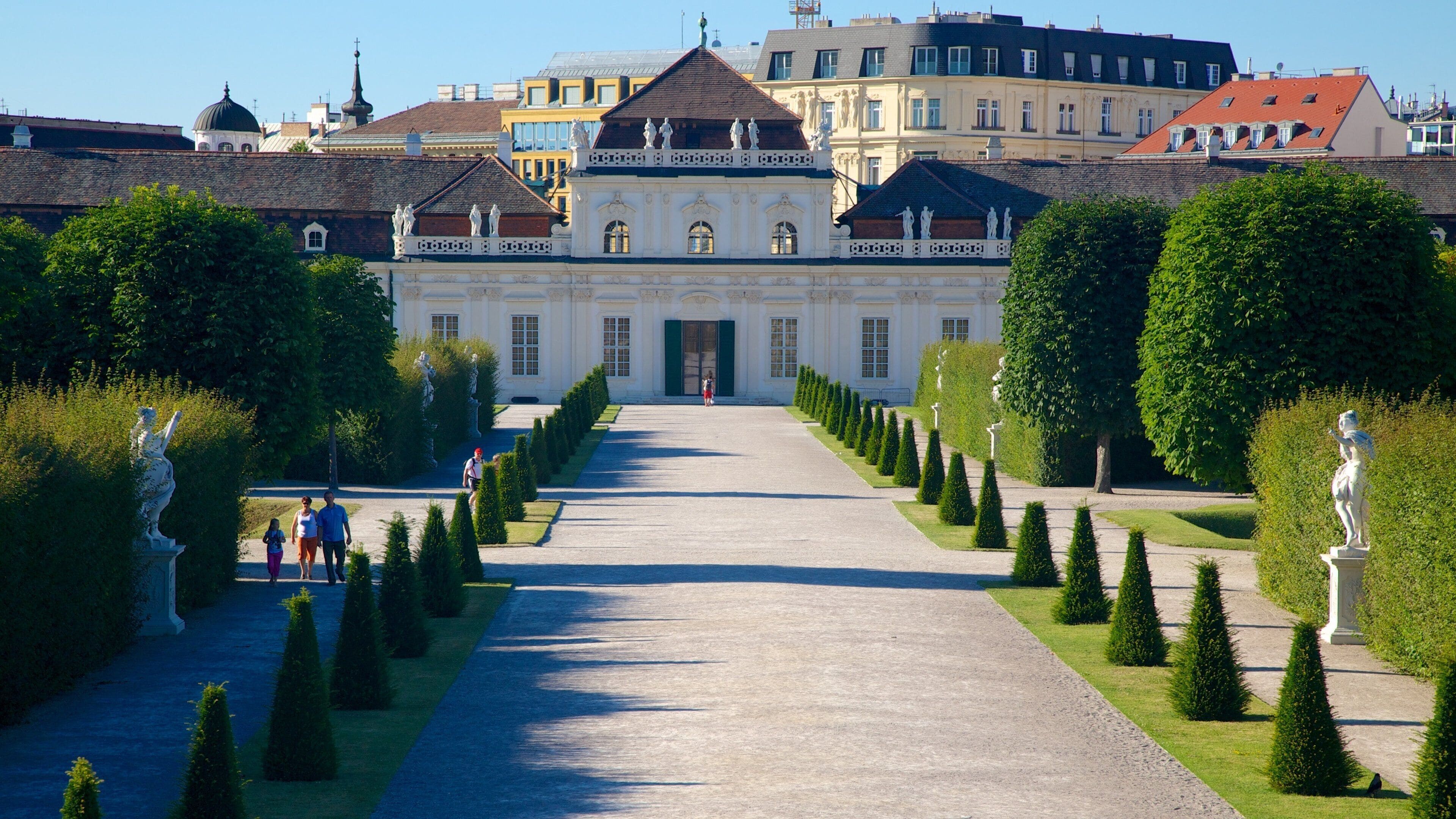 Ein prachtvolles Gebäude mit symmetrischer Fassade, einem zentralen Eingang und einem formalen Garten mit geschnittenen Hecken und Statuen.