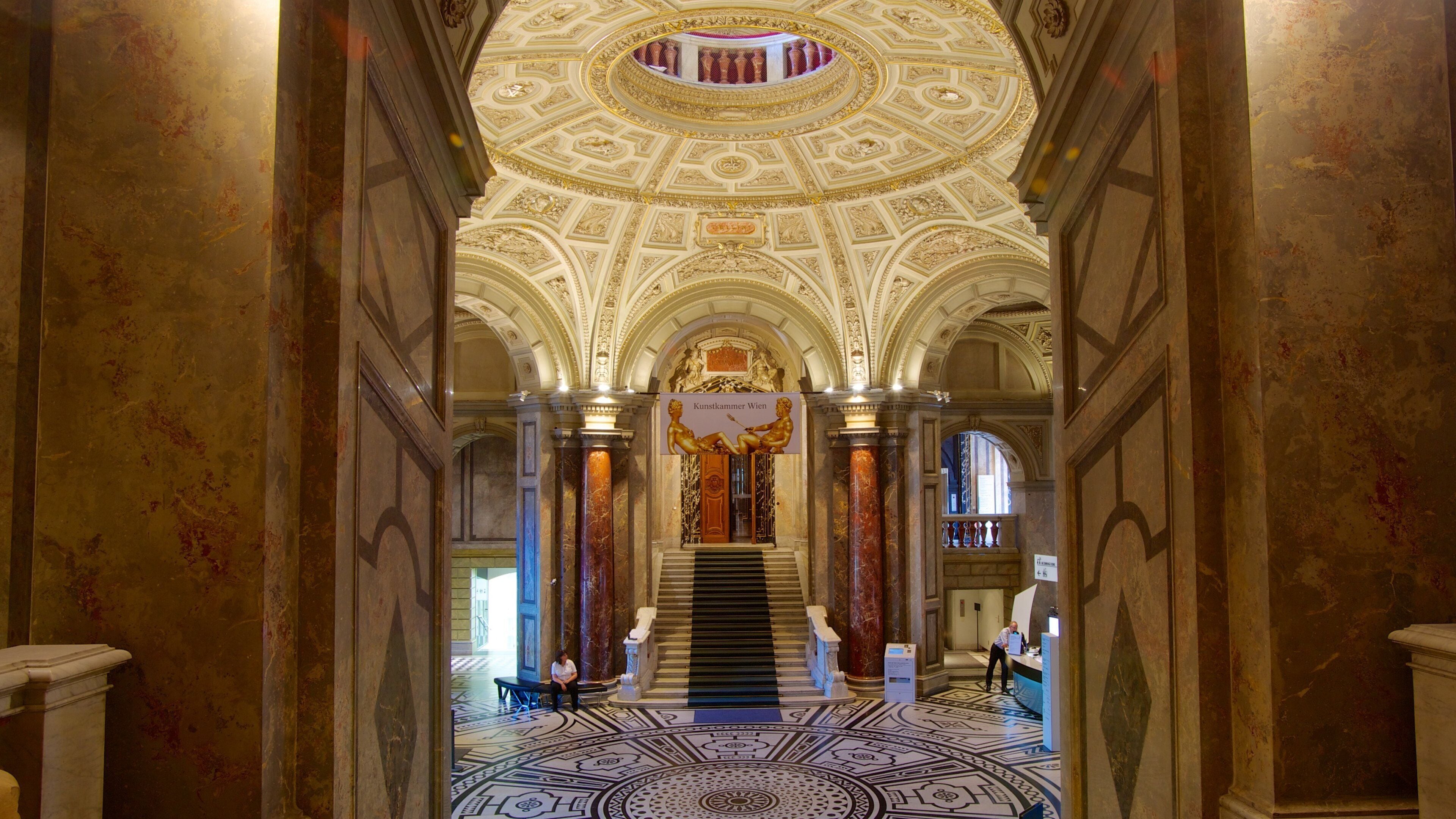 An ornate interior with a grand staircase, marble columns, and a detailed ceiling.