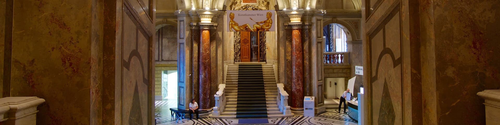 An ornate interior with a grand staircase, marble columns, and a detailed ceiling.