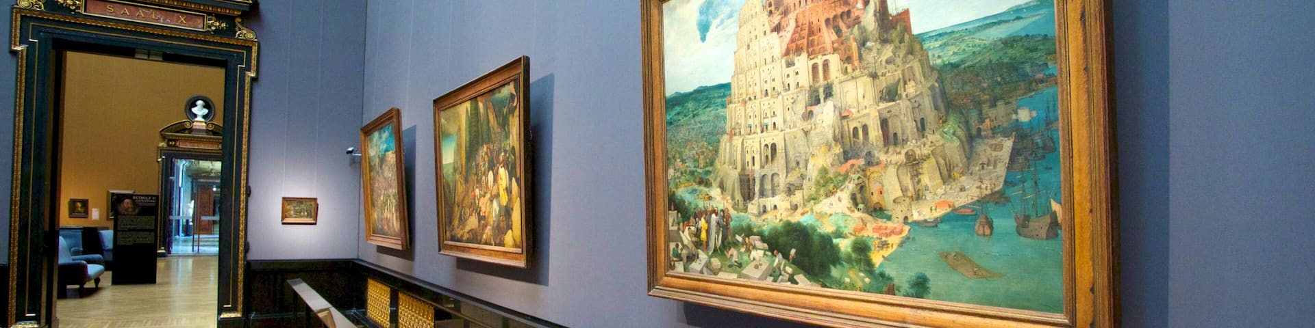 A museum corridor with large paintings and a bust on the wall.