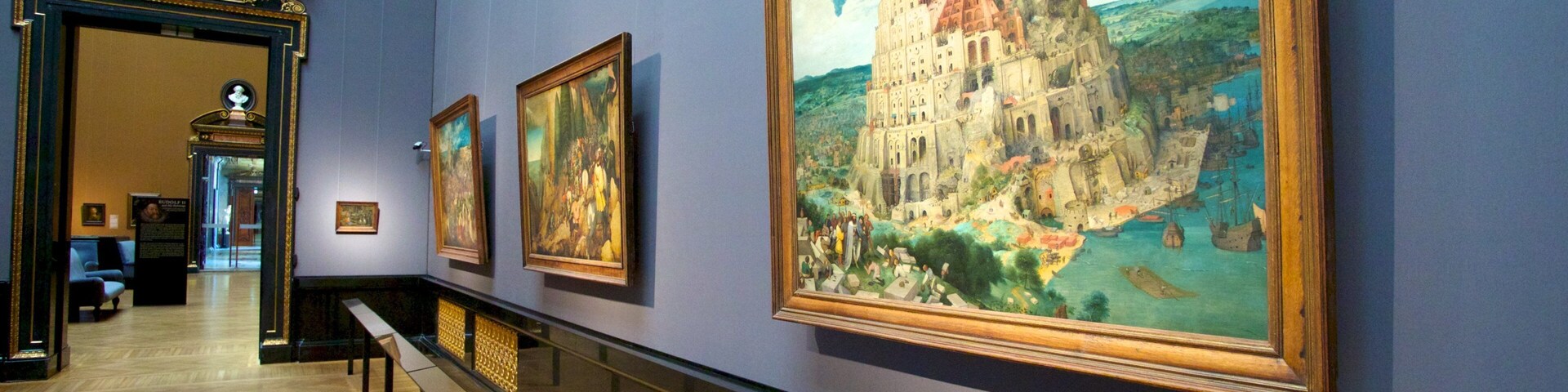 Un pasillo de museo con pinturas grandes y un busto en la pared.