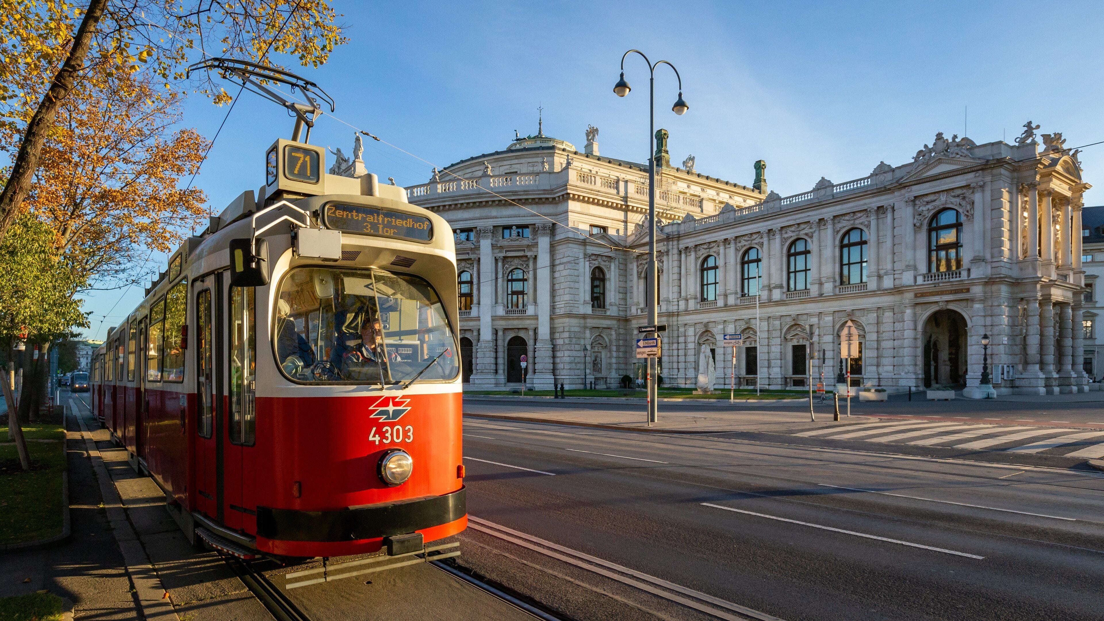 A red tram with the number 4303 on a track, passing by a historic building with classical architecture.