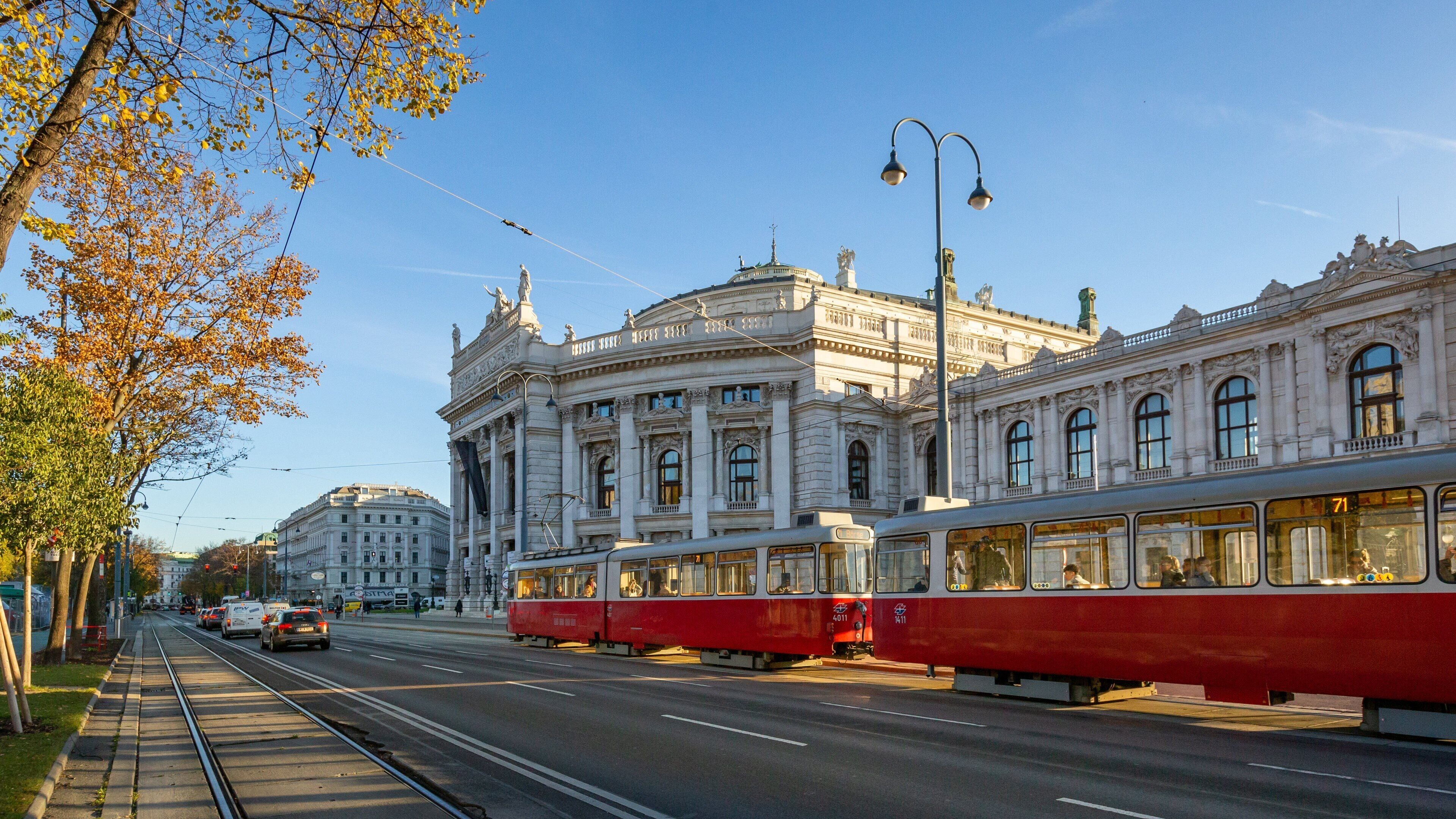 A tram on a city street with historic buildings and autumn trees.