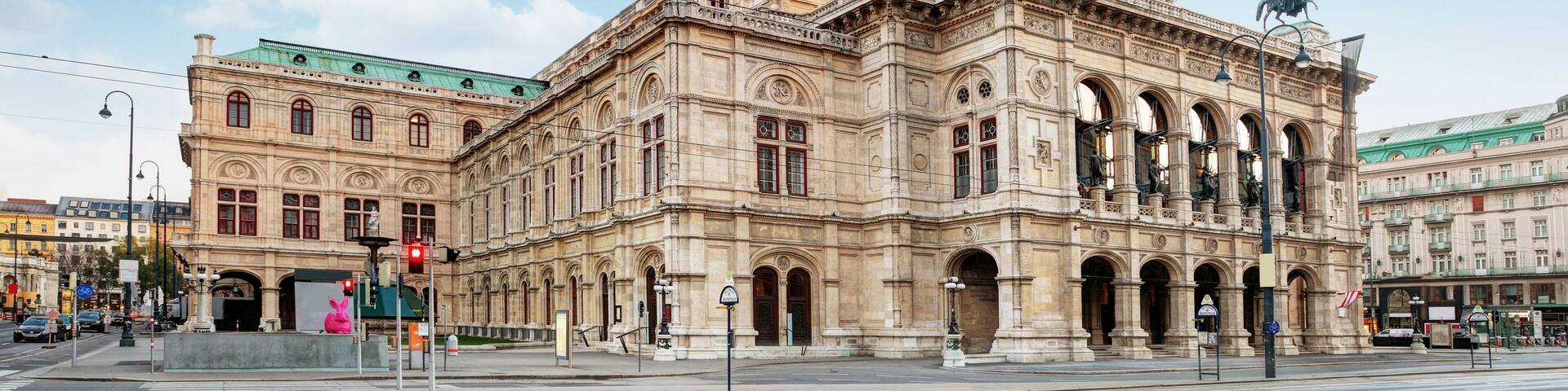 A historic building with classical architecture, large arched windows, and statues on the roof.