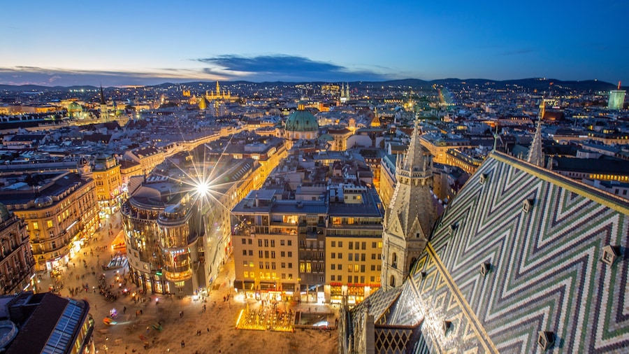A panoramic view of a city at dusk with illuminated buildings and a prominent dome structure.