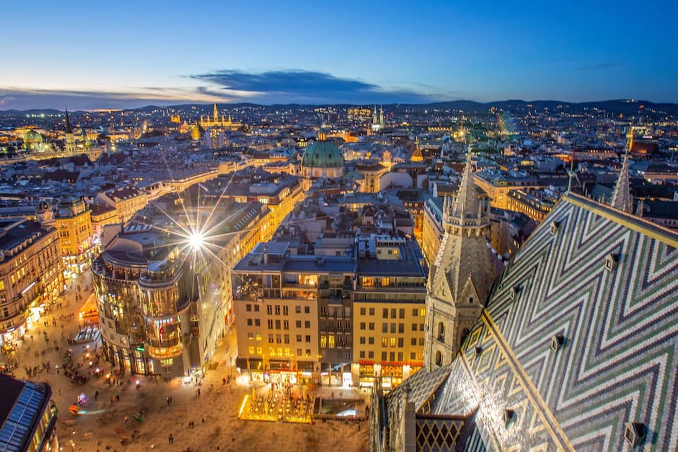 A panoramic view of a city at dusk with illuminated buildings and a prominent dome structure.