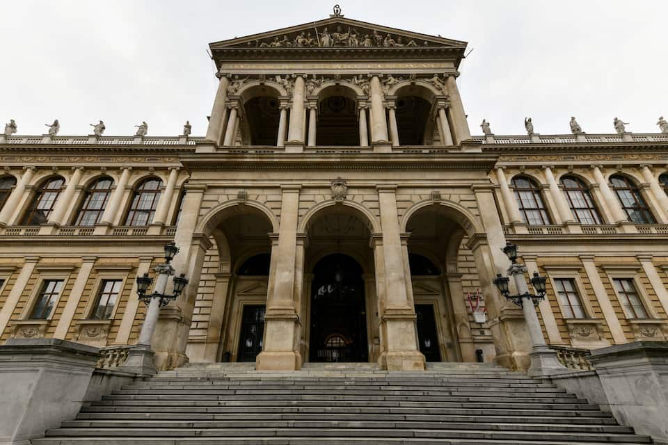 A grand neoclassical building with a symmetrical facade, large central arches, and statues on the roofline.