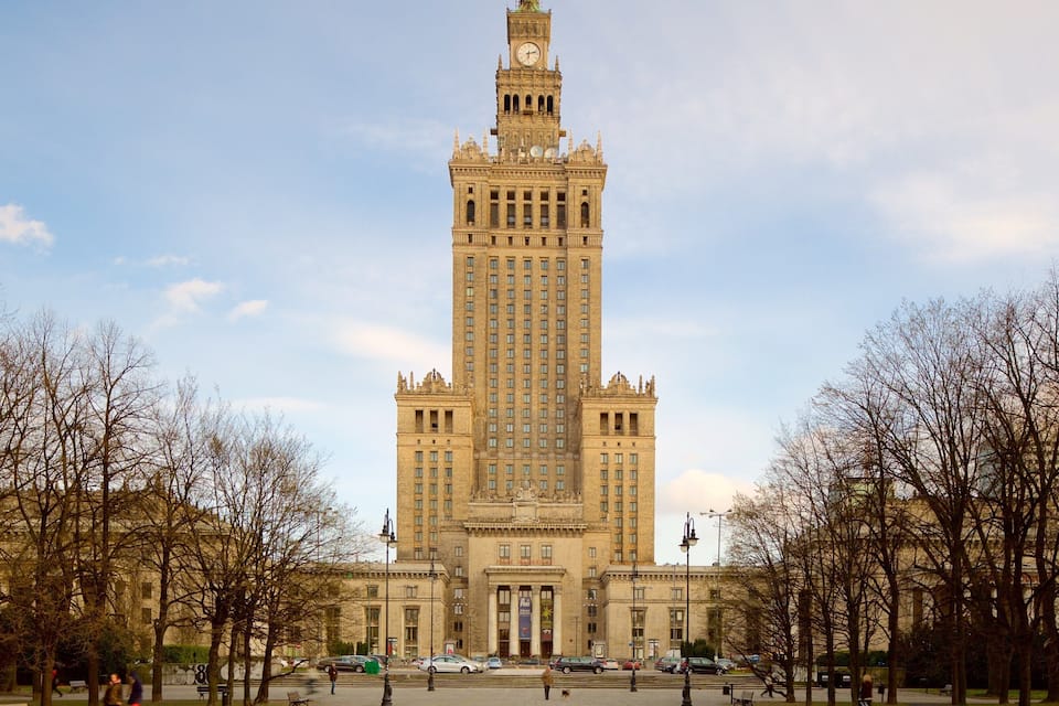 A large, historic building with a clock tower, surrounded by leafless trees and a clear sky.
