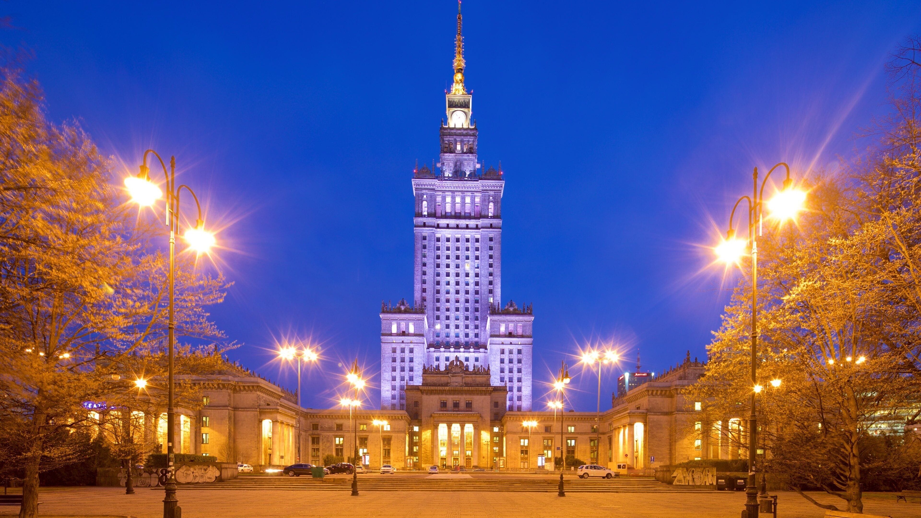 A grand building with a tall spire, surrounded by trees and street lamps.