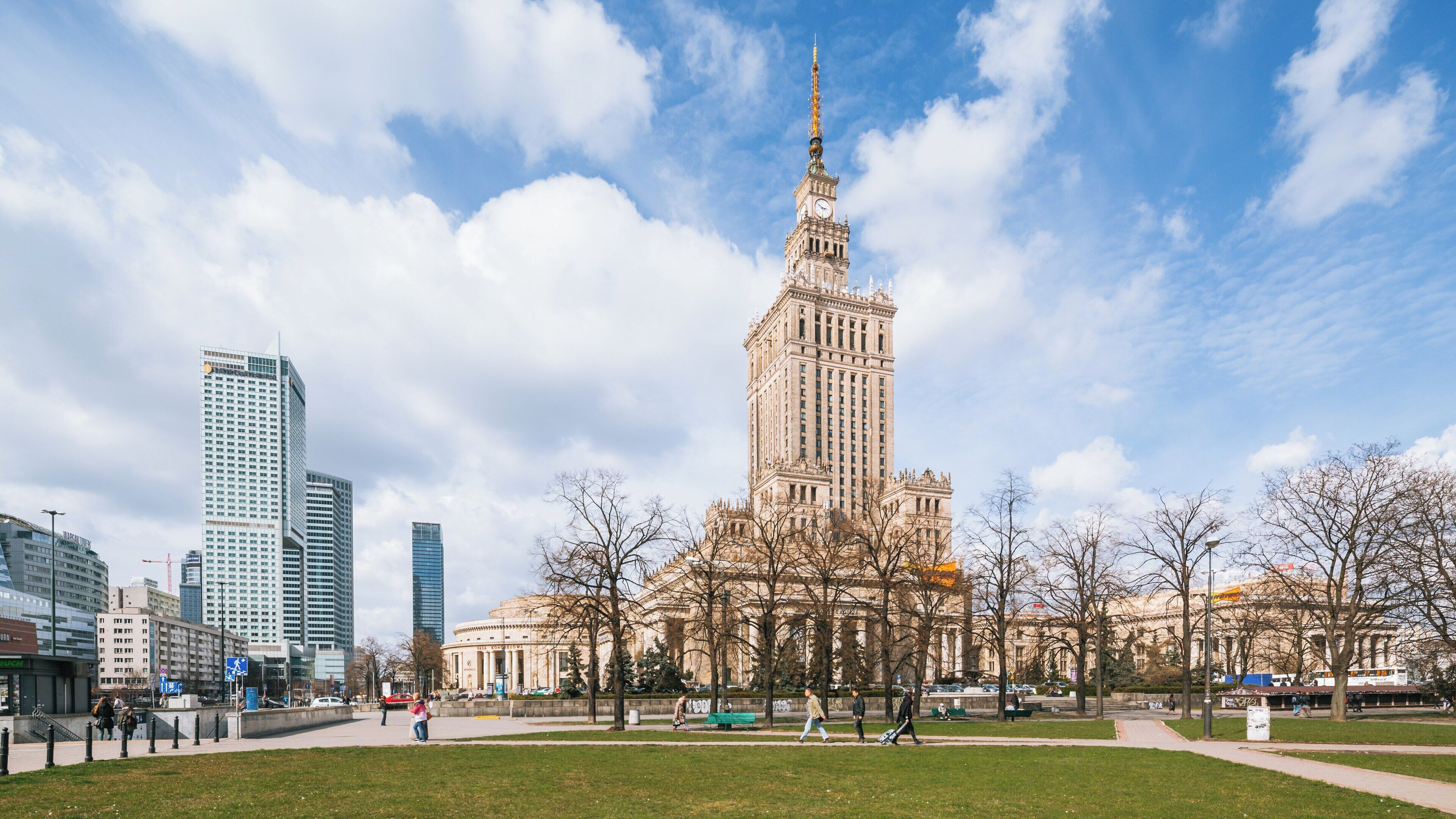 Palace of Culture and Science stands tall in Srodmiescie, Warsaw, under a beautiful blue sky surrounded by modern architecture