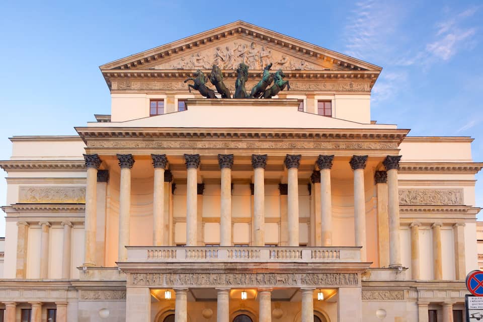 Un edificio neoclásico con frontón central, columnas y una escultura de caballos.