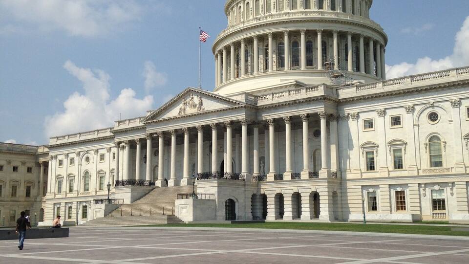 A large white domed building with columns, a flag, and a statue on top.
