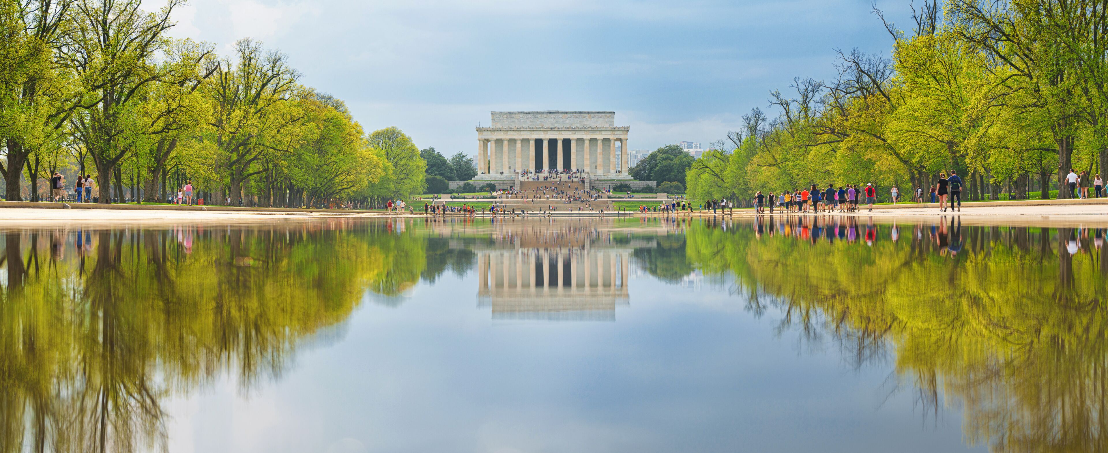 O Memorial Lincoln refletido em águas calmas, rodeado por árvores verdes e um céu claro.