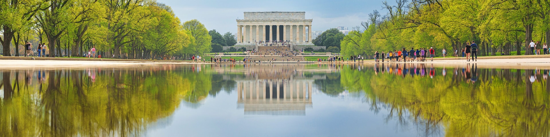 O Memorial Lincoln refletido em águas calmas, rodeado por árvores verdes e um céu claro.