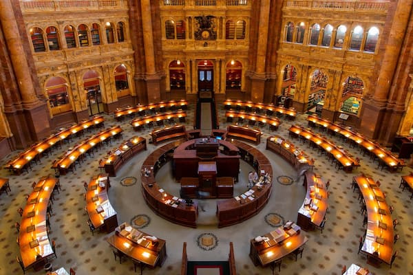Um salão amplo com uma mesa circular central, rodeada por fileiras de mesas e cadeiras.