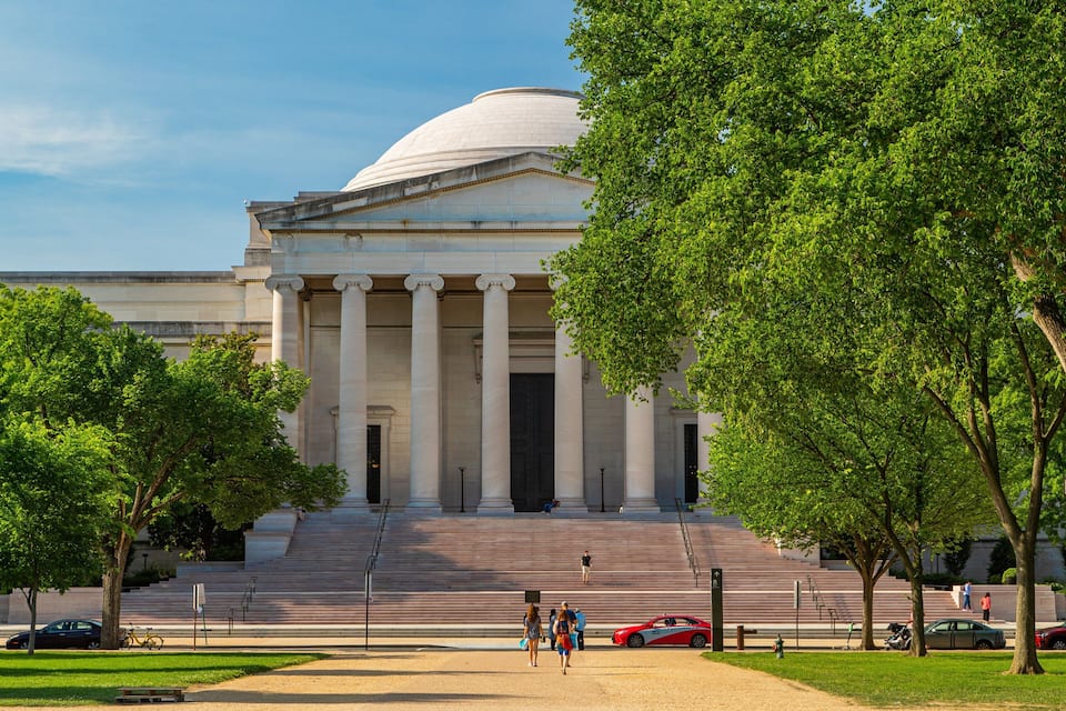 A large neoclassical building with a dome and columns, surrounded by trees and a grassy area.