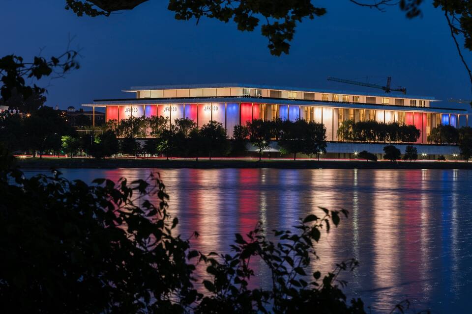 A modern building with illuminated panels and a reflection in the water.