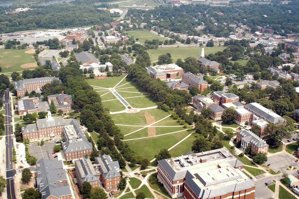 An aerial view of a university campus with multiple buildings, green fields, and a central open space.