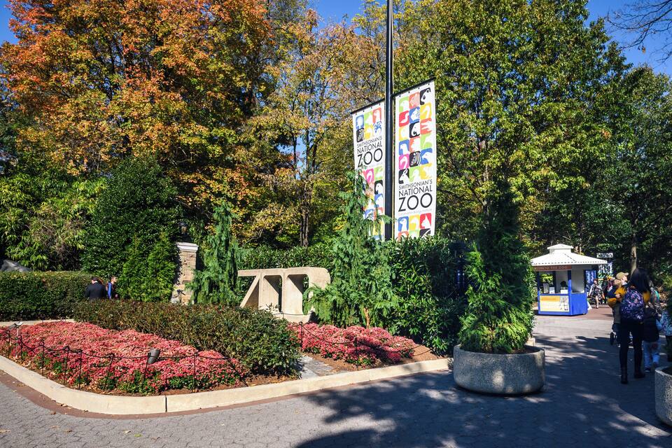 A zoo entrance with signage, a kiosk, and landscaped gardens.