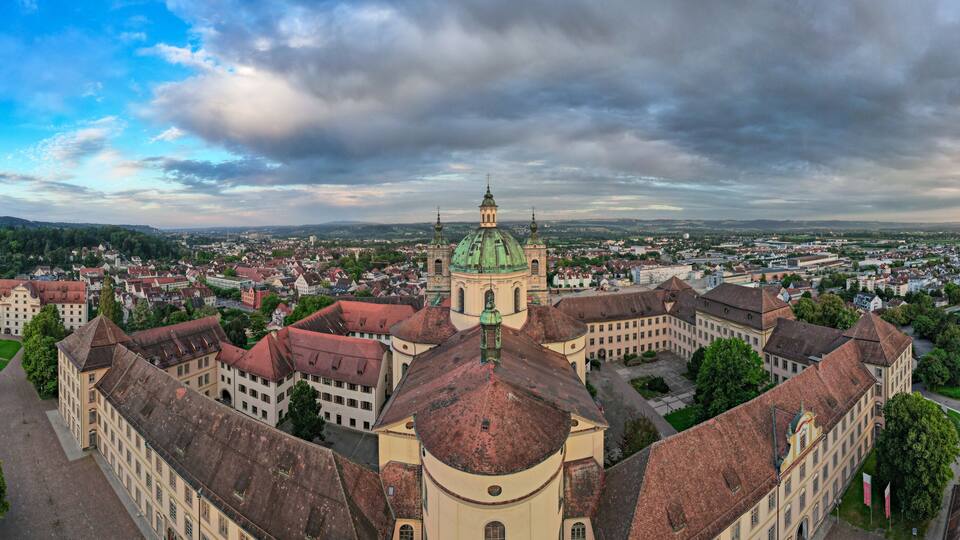 A historic cityscape with a prominent church featuring a green dome and red-tiled roofs.