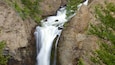 A waterfall cascading down a rocky cliff surrounded by green foliage.