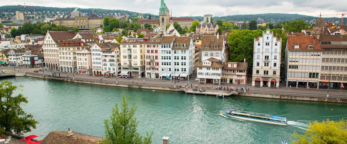 A river with a boat, surrounded by historic buildings and a prominent church spire.